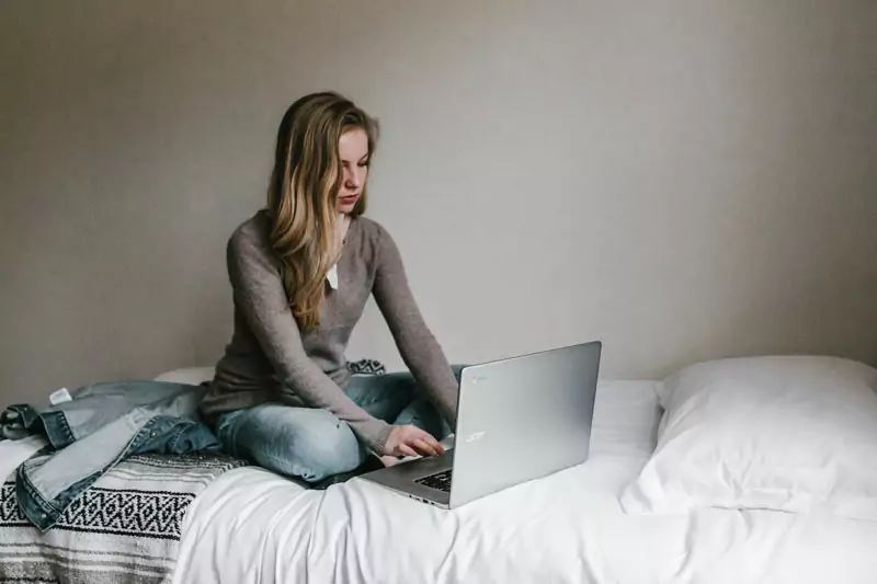 Junge Frau sitzt mit Laptop auf dem Bett